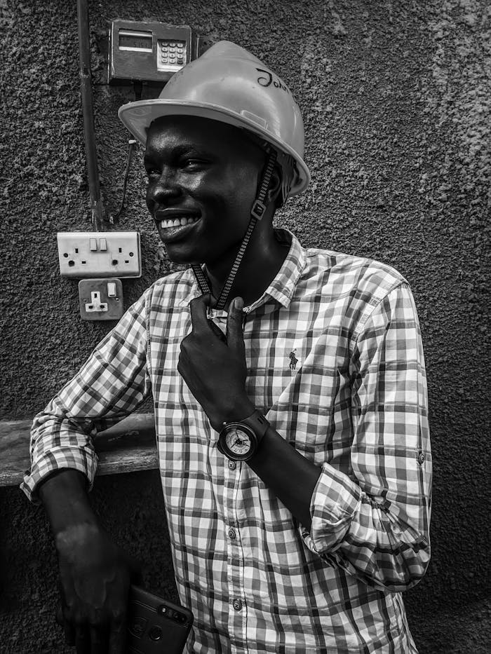 Smiling worker in a safety helmet, captured in a monochrome setting, with a confident pose.